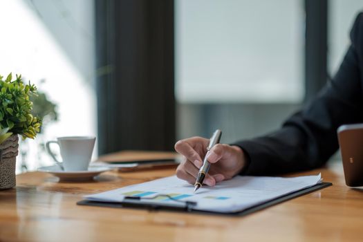 Close up hand of business woman analyst pointing with pen on paperwork graph chart financial report on wooden desk.