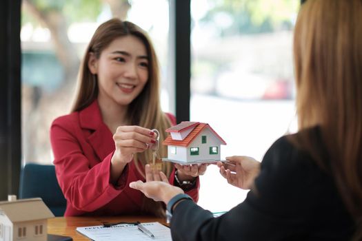 Real estate agent holding house key to his client after signing contract agreement in office,concept for real estate, moving home or renting property