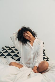 Young mixed race woman stretching neck in bed. Copy space. Vertical image. Healthy lifestyle concept.