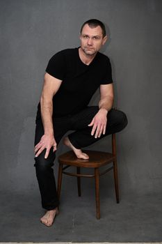 Vertical portrait of an adult man sitting on a chair in the studio on a gray background