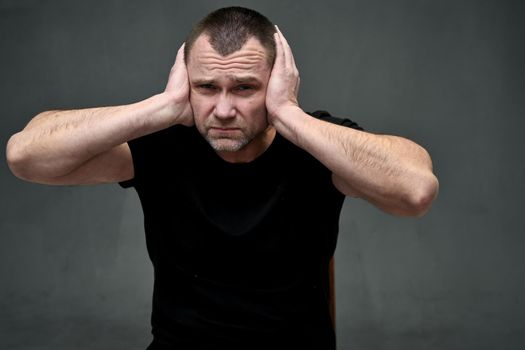 Close-up portrait of a man does not hear, covering his ears with his hands with displeasure