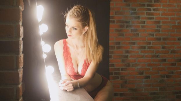Young blonde woman in red underwear looking at mirror - posing for photographer, close up