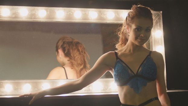 Young blonde woman in blue underwear looking at mirror - posing for photographer, close up