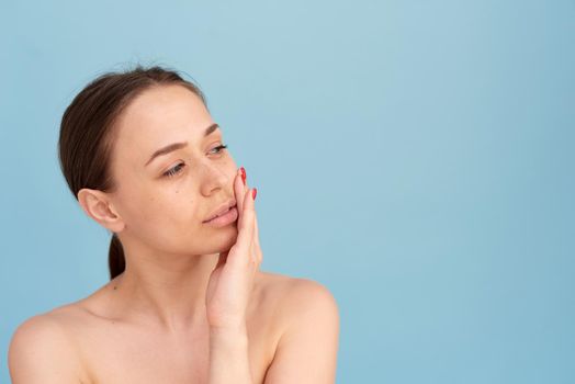 Skin care. Beautiful smiling female model with natural makeup with glowing moisturized skin on a blue background close-up.