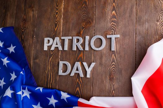the words patriot day laid with silver metal letters on wooden board surface with crumpled usa flag below