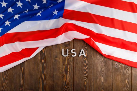the word USA laid with silver metal letters on wooden board surface under crumpled flag of United States of America in directly above perspective
