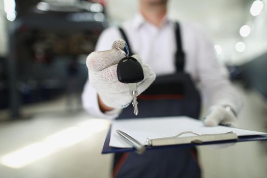 Close-up of service worker give keys from fixed automobile to owner and hold paper for sign. Car service, professional mechanic, garage, pit stop concept