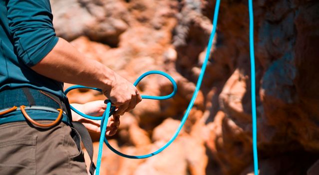 A young man prepares for rock climbing in the mountains outdoor, an athlete ties a figure eight loop on a rope during training, mountaineering on a sunny day, close-up view.
