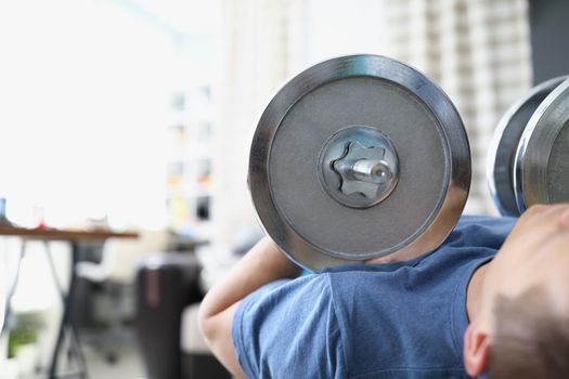 Close-up of man lift heavy metal dumbbell laying on training machine. Train body for muscles, healthy living, gym at home. Sport, active lifestyle concept