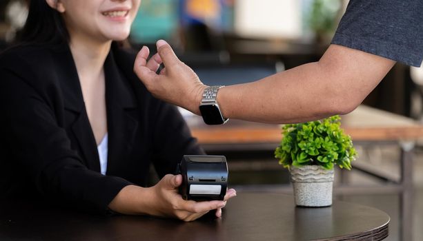 Cropped image of Businessman making a payment by using a smartwatch with blurred cafe as background. NFC technology concept.