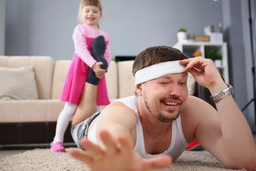 Low angle of girl child pull fathers foot and want to play, tired man lay on floor carpet. Active and happy kid on holiday bored at home. Childhood concept