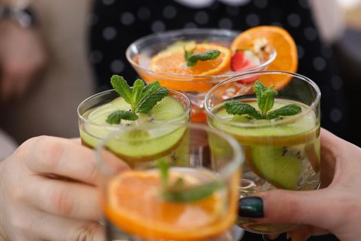 Close-up of group of people with cooling drinks make clink with glasses, raise toast. Summer fruit beverages, tasty alcoholic drinks. Party, fun concept