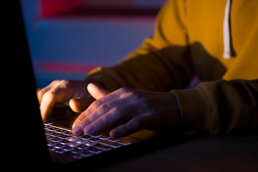 Male hands are typing on a laptop keyboard, a man works, develops a business, studies, plays a computer game at night. Close-up view.