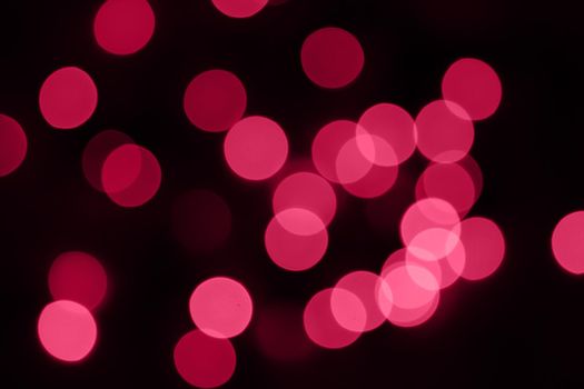 Defocused bokeh lights on black background, an abstract naturally blurred backdrop for Valentine's Day or birthday party. Festive light texture. Pink and red garland in blur. Overlay effect for design