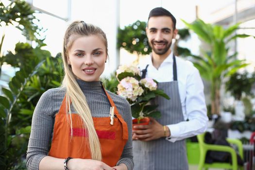 Portrait of female flower studio consultant ready to help you with choice, guy on background hold finished bouquet. Floral, flower, plant, creative concept