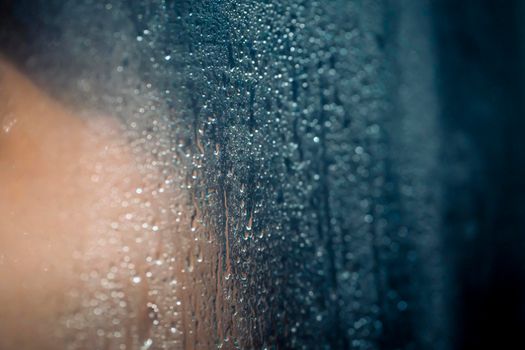 Large and small drops of water on the glass of a modern shower stall, a person takes a shower, a close-up view of the splashing water, a banner with copy space.