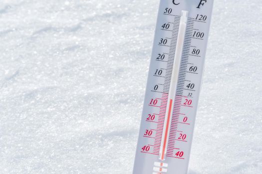 The thermometer lies on the snow in winter showing a negative temperature.Meteorological conditions in a harsh climate in winter with low air and ambient temperatures.Freeze in wintertime.Sunny winter