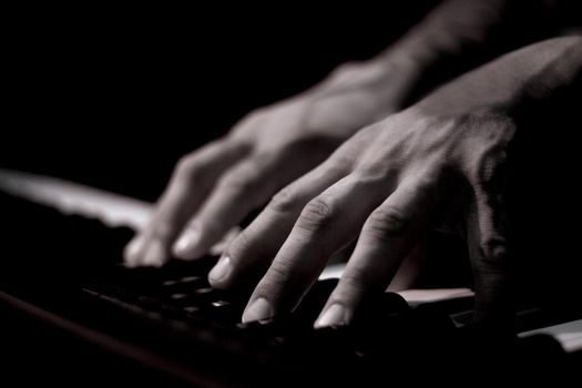 Tattooed mans hands on the keyboard of a piano. Dark background