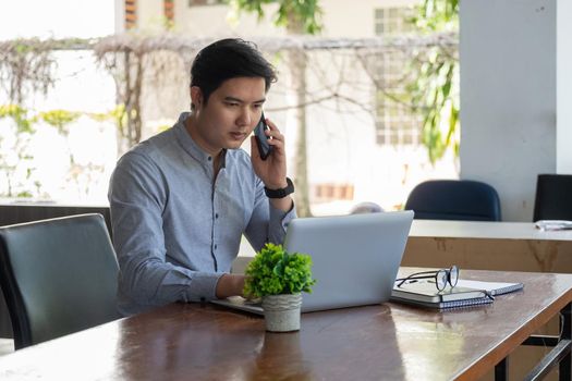Portrait of young asian man freelance online working from home with laptop computer during call phone. quaratine coronavirus, technology startup business