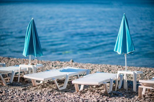 Several white sun loungers and a turquoise parasol on a deserted beach. The perfect vacation concept