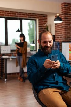 Businessman holding modern smartphone browsing on social media texting with remote friend in startup company office. Manager searching business information developing online communication app.