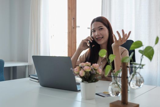 Portrait of young asian woman freelance online working from home with laptop computer during call phone. quarantine coronavirus, technology startup business.