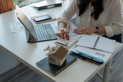 Close up hand of Business asian woman using calculating interest, taxes and profits to invest in real estate and home buying