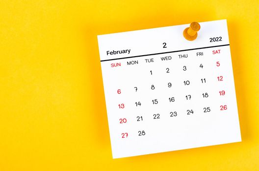 The February 2022 and wooden push pin on yellow background.