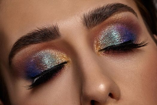 Face of a girl with luxury makeup and perfect skin. She has closed her eyes. Blue and golden eyeshadow, false eyelashes and brown eyebrows. Professional maquillage. Close up