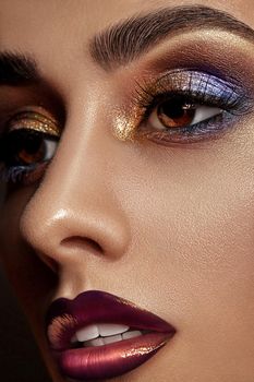 Gorgeous brunette model with luxury makeup and perfect skin is looking aside. Multi-colored eyeshadow, false eyelashes, glossy purple lips. Professional maquillage. Close up