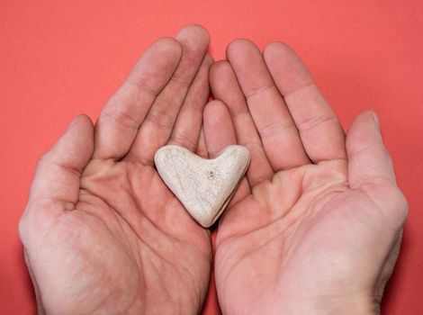 Male hands hold a heart-shaped stone on a red background, close-up. romantic valentine's day gift.