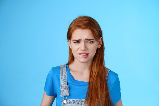 Uneasy upset redhead girl feel uncomfortable, stare frustrated, biting lip frowning, pull sad face upset, apologizing friend, express pity dilsike, stare doubtful uncertain, make bad choice.