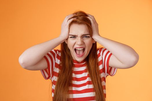 Pissed fed up redhead female teenager annoyed, break down, grab head yelling hateful displeased, depressed, upset failure, stand angry disappointed, panic, shouting aggressive orange background.