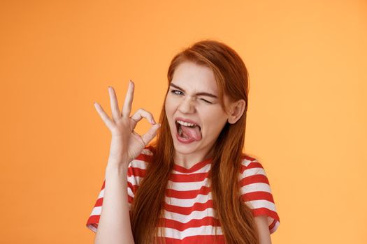 Sassy asserive relaxed redhead woman assuring everything under control, make deal, wink show tongue silly accepting terms, judgemental approval gesture, like idea, show okay excellent sign.