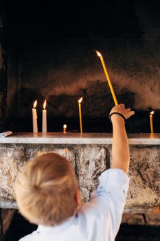 Boy puts a wax candle in a niche in a temple. High quality photo
