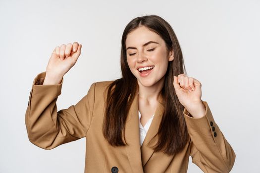Successful businesswoman, saleswoman dancing and having fun, wearing office suit, posing over white background.