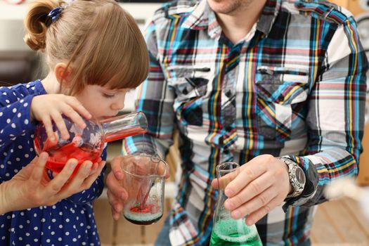 Man and little girl are playing colorful liquids in flasks. Research equipment with color reagent or food additives at home concept