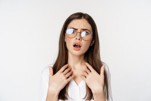 Offended and upset young woman in glasses, beeing jealous or disappointed, feeling hurt, grimacing and sulking, standing confused over white background.