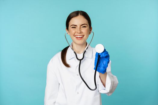 Image of woman doctor, listening patient lungs with stethoscope, doing medical checkup in clinic, standing over blue background.