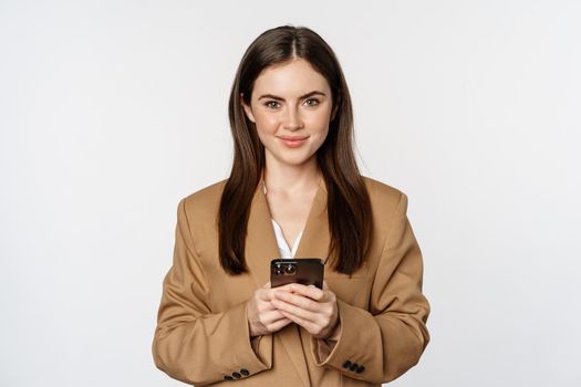 Smiling businesswoman using smartphone, app on mobile phone, standing over white background.