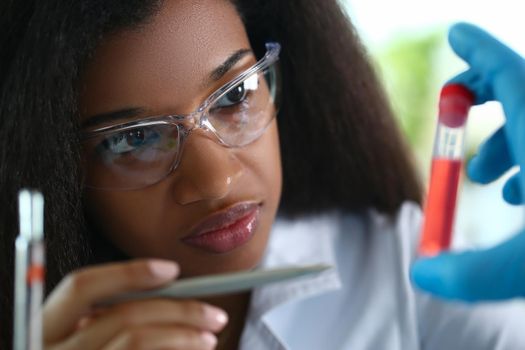 African american chemist holds glass test tube with red liquid solution. Analyzing various reagent options using a chemical manufacturing concept