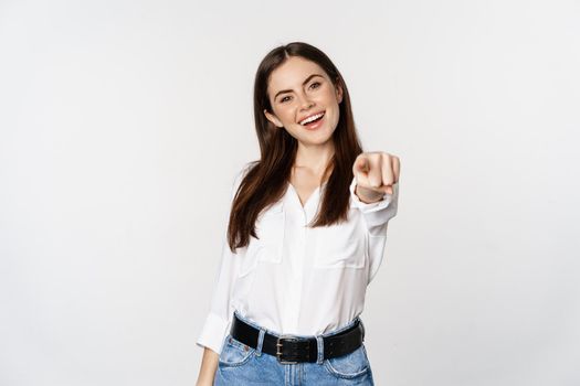 Confident young corporate woman pointing fingers at you camera, inviting, choosing, congratulating, standing over white background.