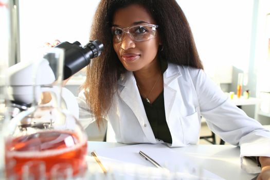 Black woman scientist in goggles, conducts study using microscope. Viral bacteria research concept