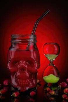 Red juice in skull jars with hourglass and dried flowers on a red background.