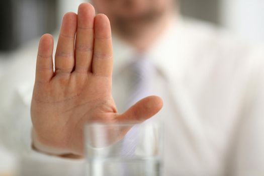 Male hand shows a negative gesture to glass beaker. Refusal of spicy alcoholic drinks concept