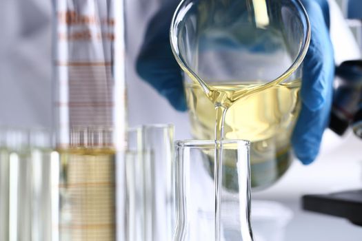 Hand pours yellow liquid into test tube. Conveyor line for the production of household cleaning products concept