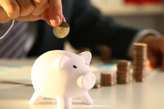 Businessman hand throws coin into piggy bank. Future requires credit education or mortgage loan concept