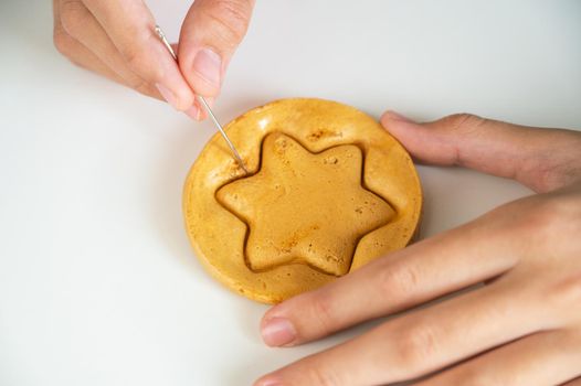 Hands closeup scratch brown sugar caramel candy cookies with a metal needle in the shape of a star on a white background.