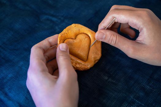 Hands closeup scratch brown sugar caramel candy cookies with a metal needle in the shape of a heart on a white backgound
