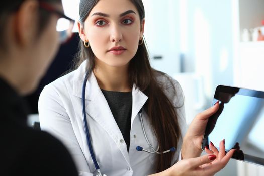 Beautiful female medical doctor explains diagnosis to patient holding and showing digital tablet pc. Medical consultation concept